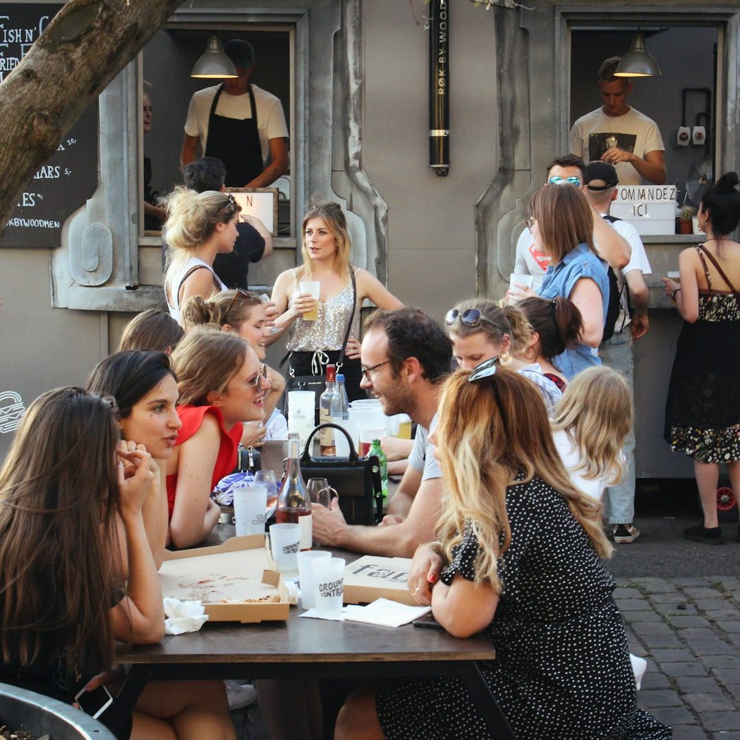 Groupe de personnes assises à une table en extérieur, partageant un repas et discutant.