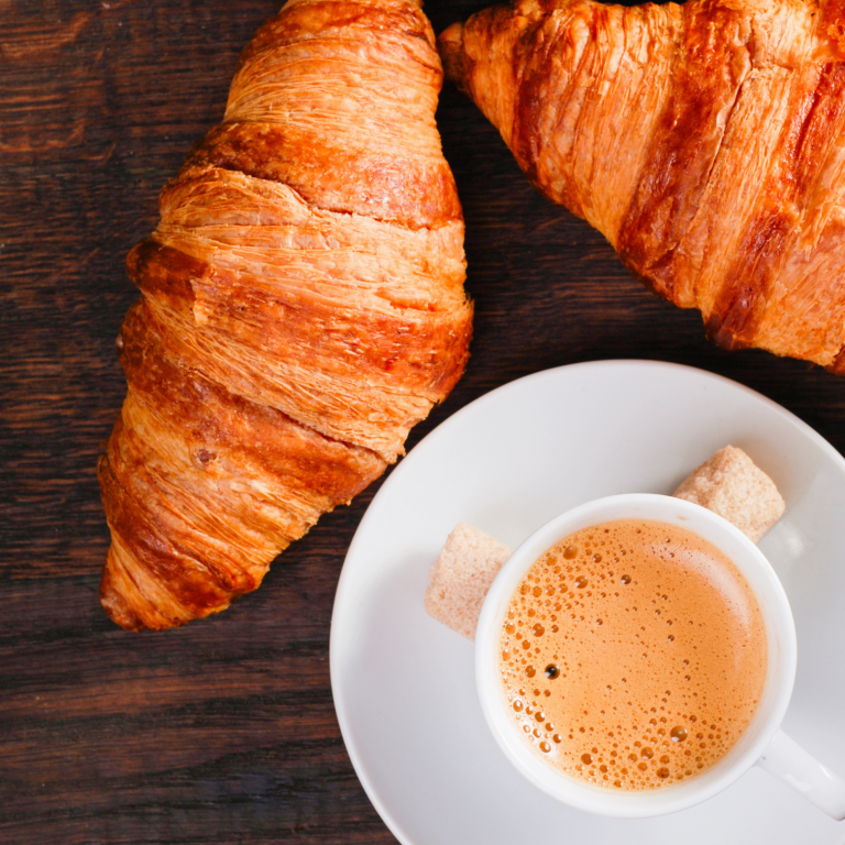 Croissants dorés accompagnés d'une tasse de café sur une table en bois.