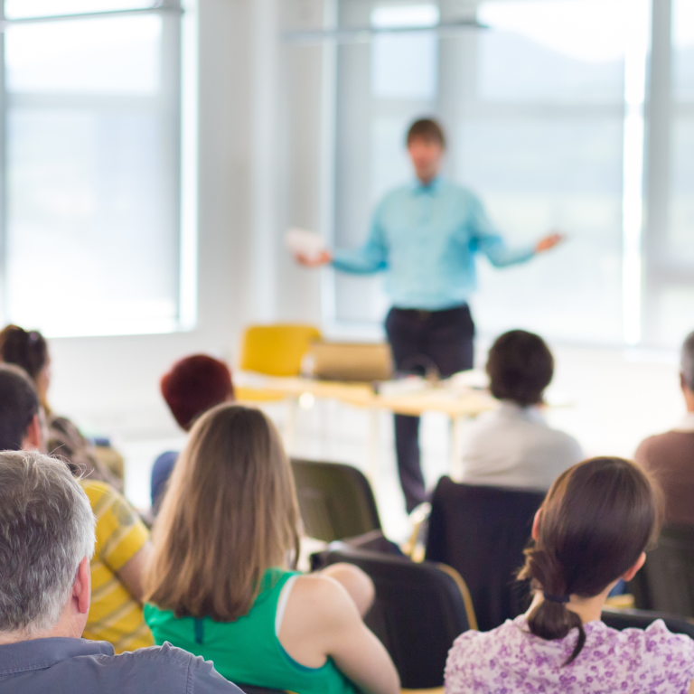 Un conférencier devant un public attentif dans une salle lumineuse.